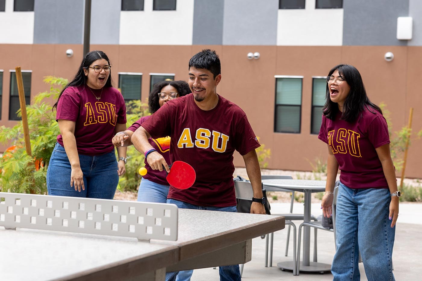 Four ASU students in maroon shirts play table tennis in a campus courtyard, reflecting the fun explored in the Community Sports Management minor.