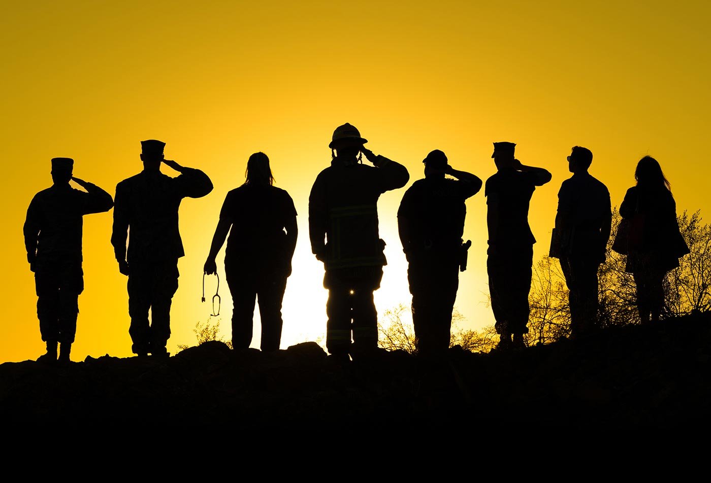 Students in uniform salute against a vibrant sunset, symbolizing commitment and teamwork in ASU’s Emergency Management certificate program.