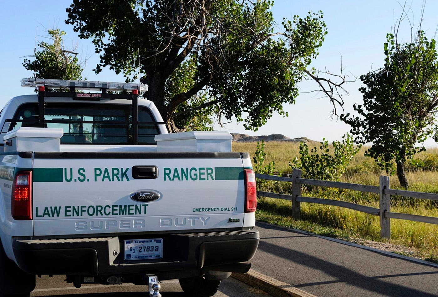 A U.S. Park Ranger vehicle parks near a grassy area, representing the field of law enforcement in parks and protected areas.