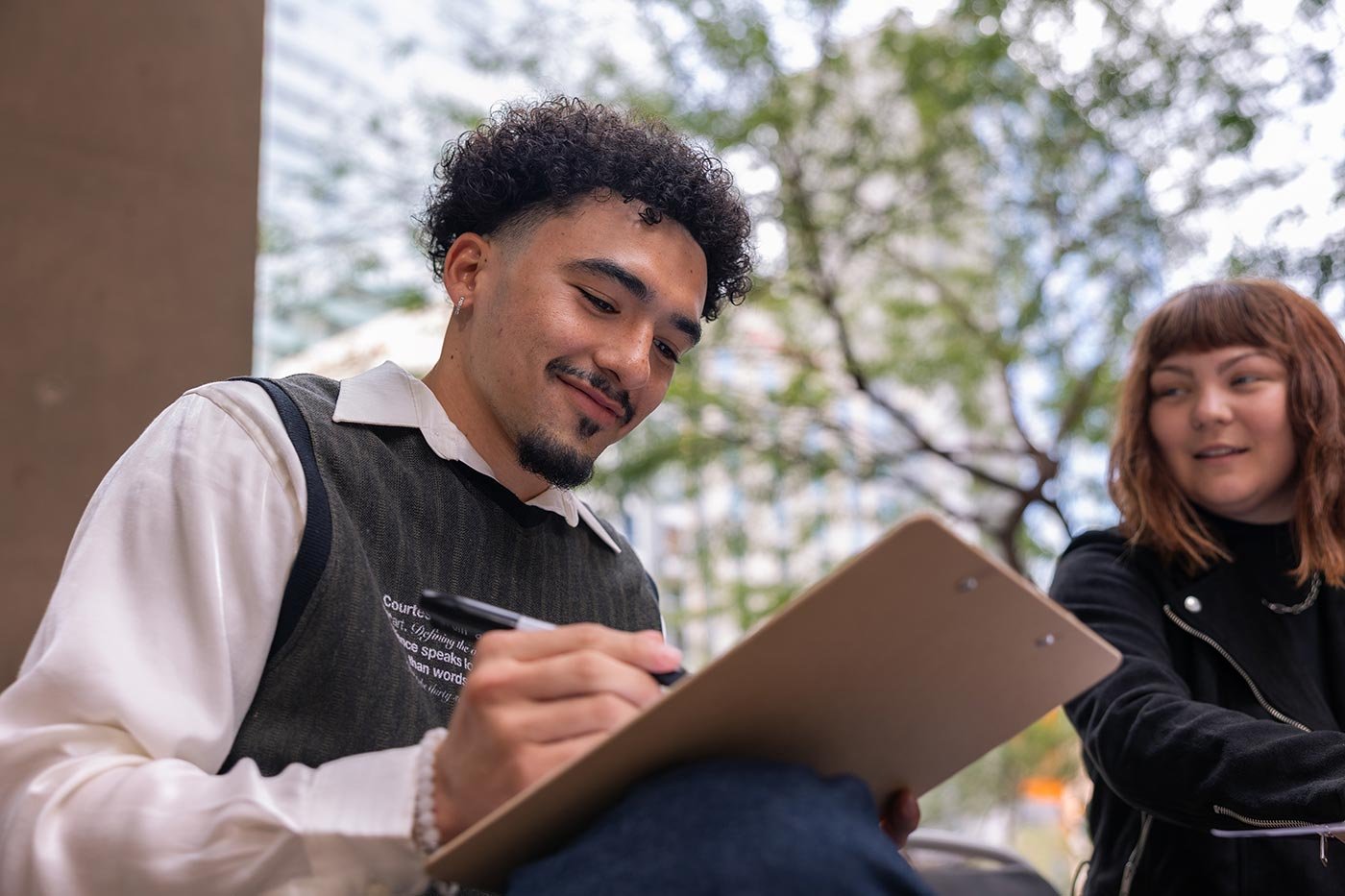 A student pursuing a minor in Nonprofit Leadership and Management writes on a clipboard while sitting outdoors with a peer.