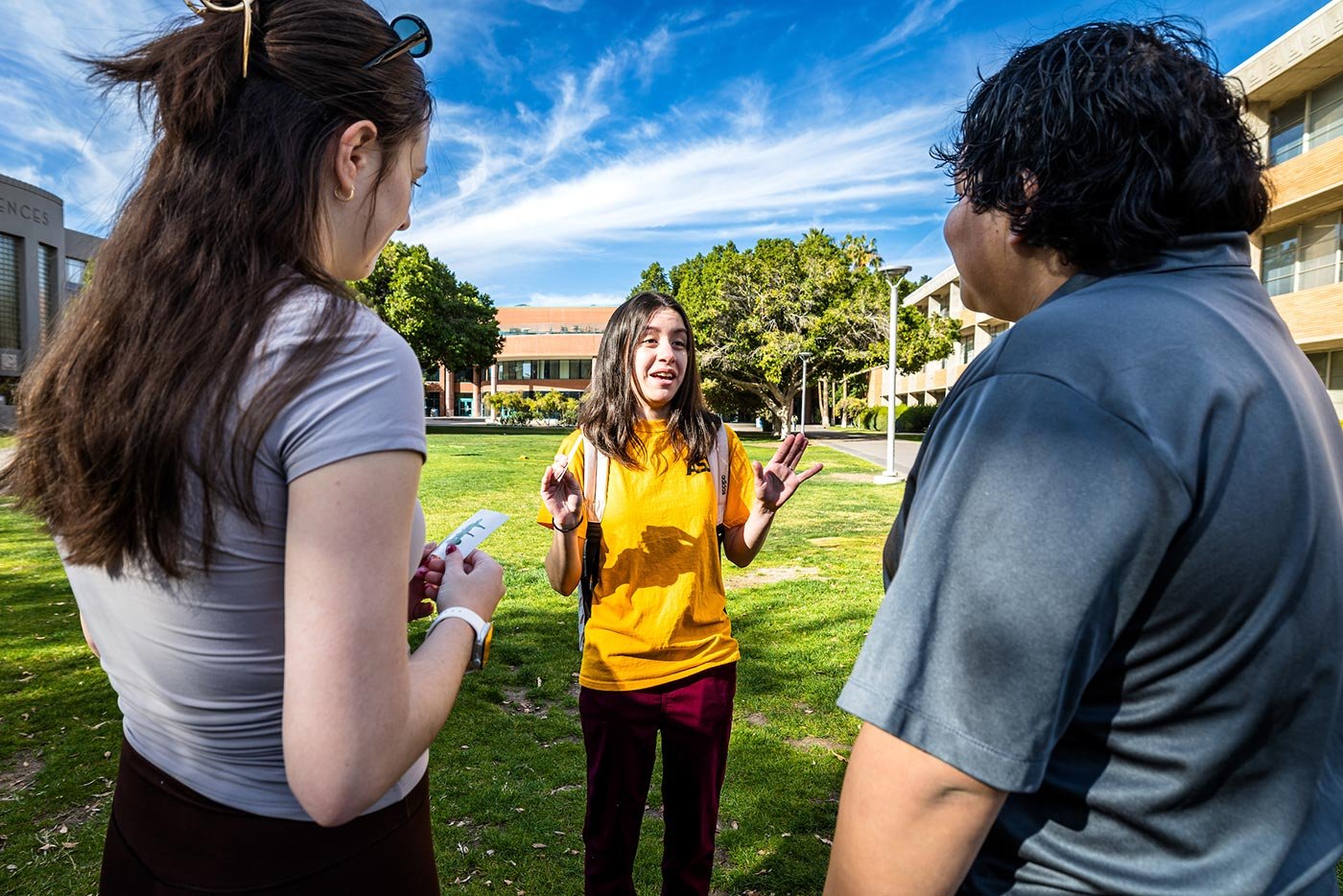 Students in the BS in Parks, Recreation and Sport Management engage in conversation outdoors, with one wearing a gold ASU shirt.