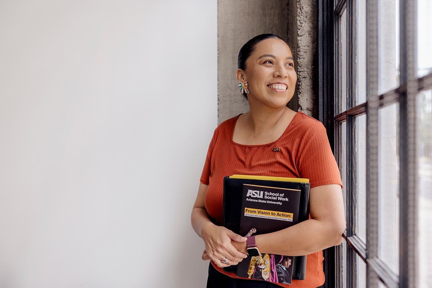 A smiling student holds essential social work materials, embodying the vibrant learning atmosphere in ASU's MSW in Social Work program.