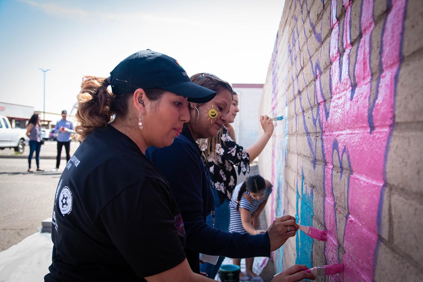 Women and children paint a vibrant mural together, reflecting the community engagement central to this ASU certificate.