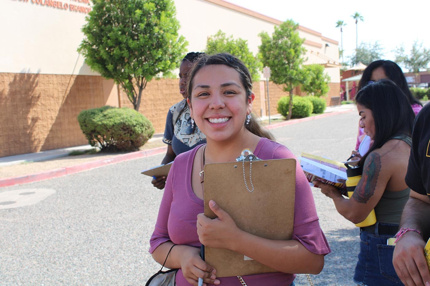 A student holds a clipboard and smiles outdoors as peers take notes nearby, reflecting teamwork in ASU's Tourism Development program.