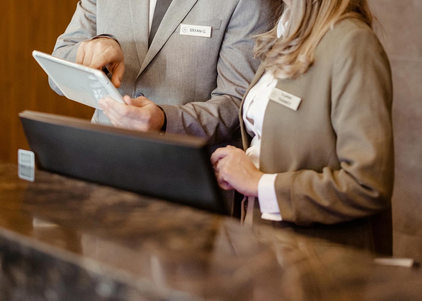 Hotel staff in formal attire engage with a tablet at a reception desk, highlighting skills relevant to the BS in Tourism Development and Management.