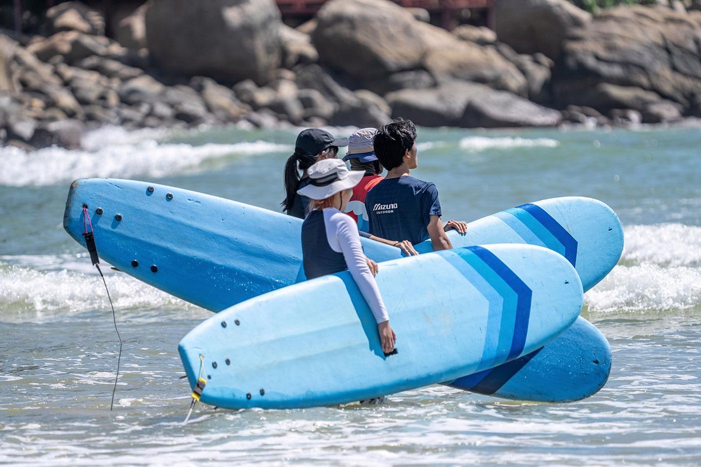 Four students carry blue surfboards along the shoreline, capturing the spirit behind ASU's Tourism, Hospitality and Event Management degree.