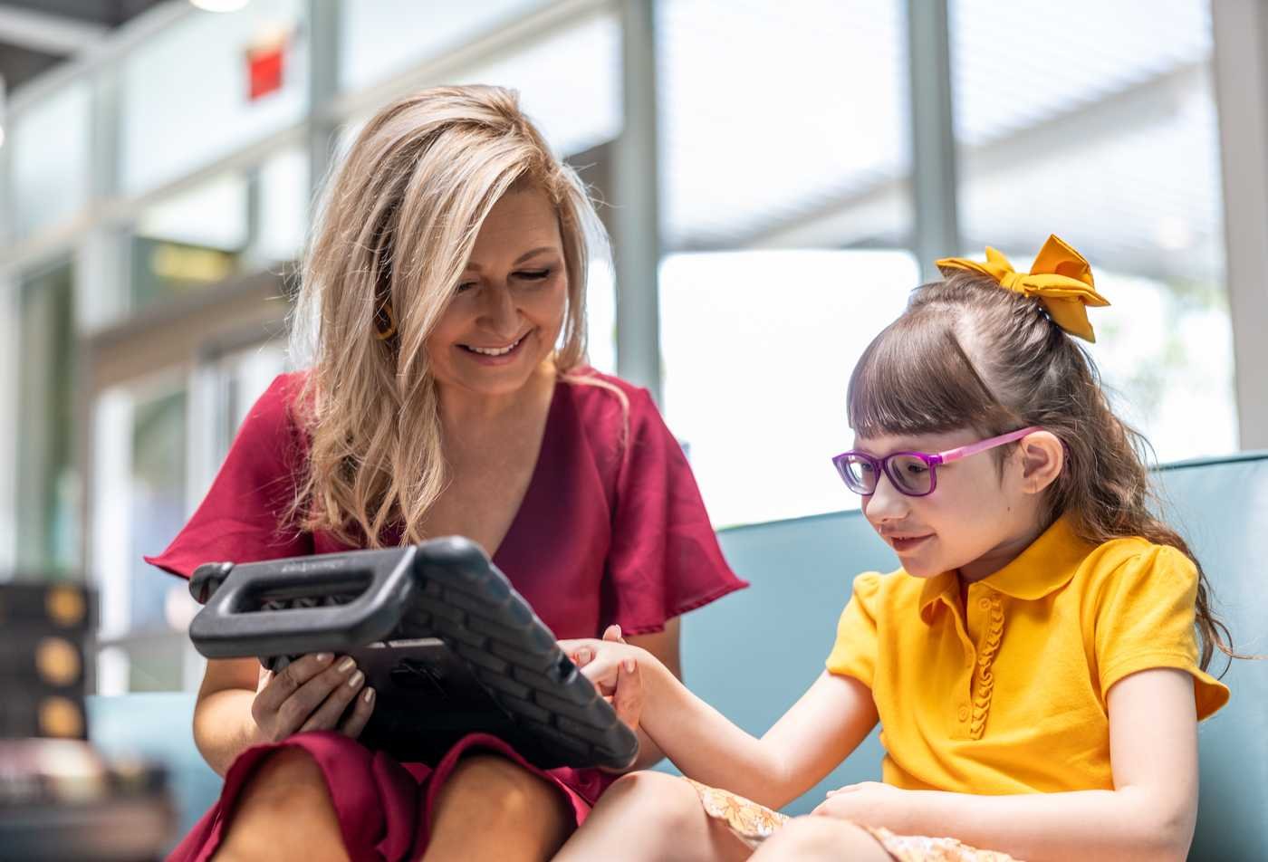 An instructor interacts with a young girl with a communication tablet, demonstrating the expertise gained in the MEd in Special Education.