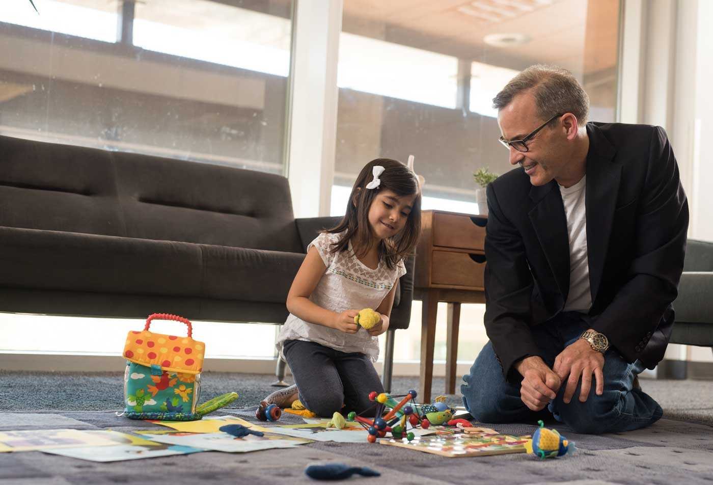 A professional plays with a young child on the floor, showcasing the community cultivated in the certificate in Applied Behavior Analysis (Graduate Certificate)