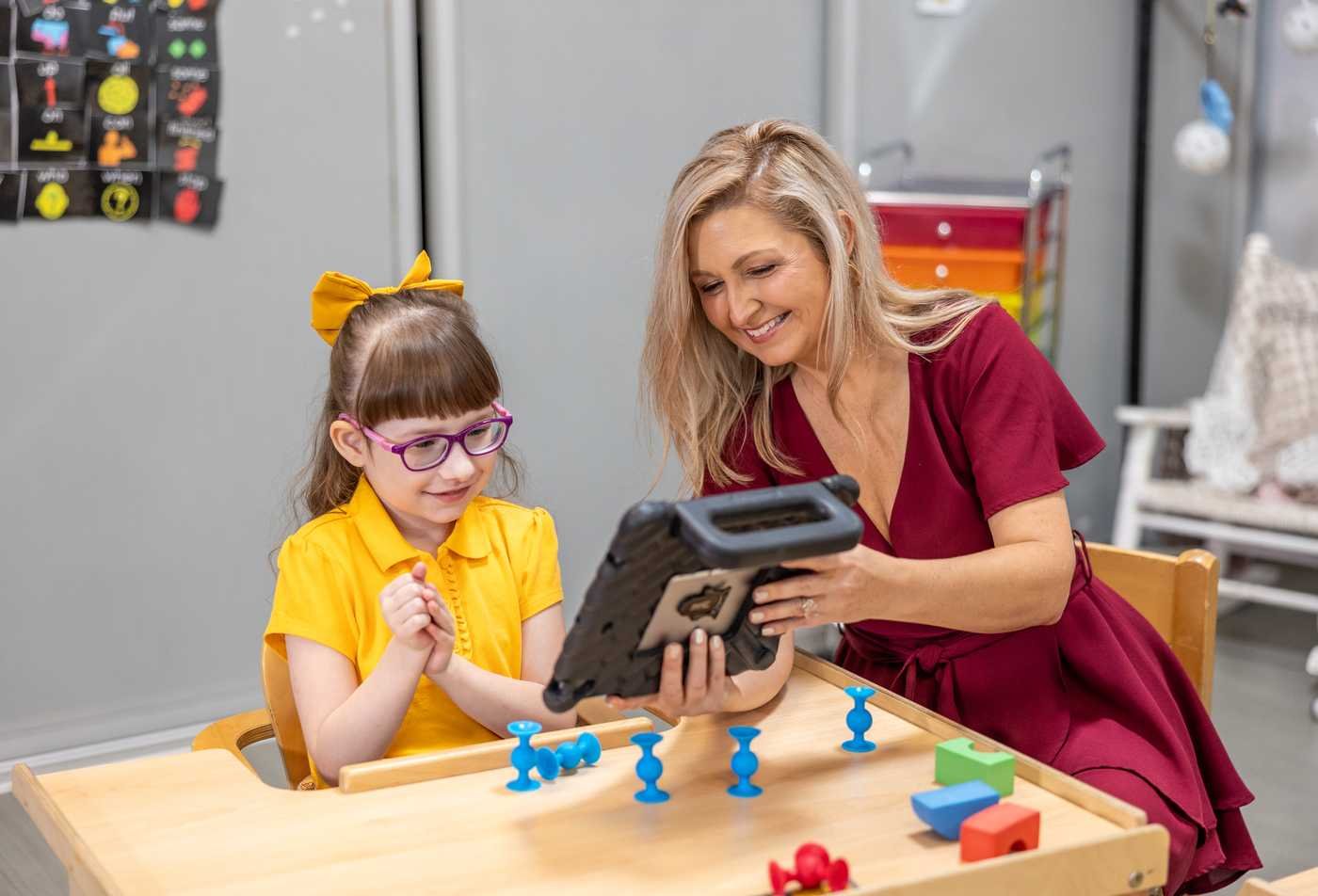 A teacher interacts with a young student with a communication tablet, demonstrating the expertise gained in the BS in Behavior Analysis.