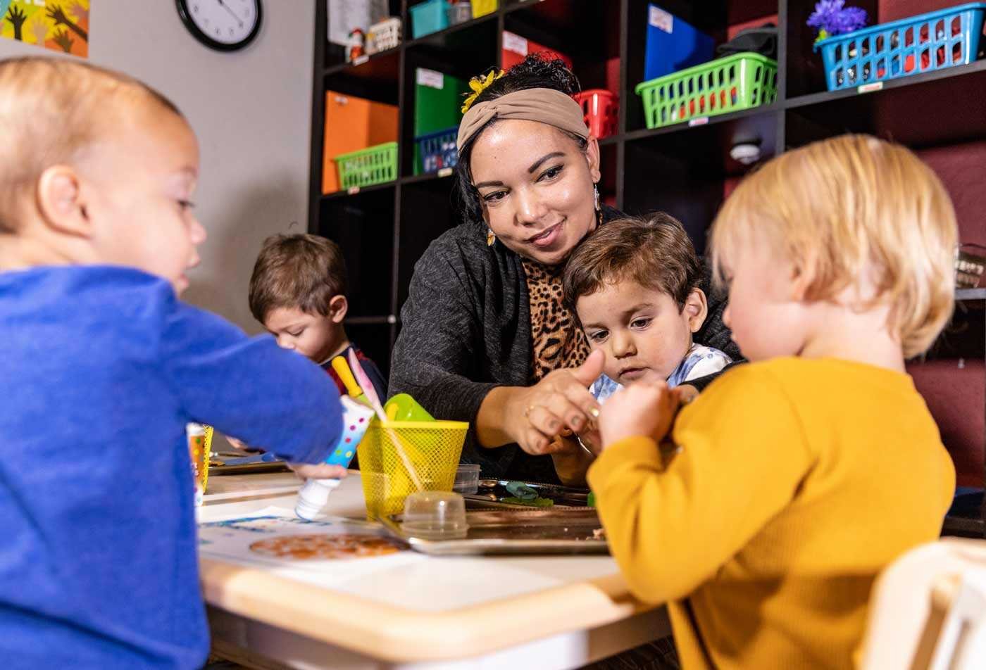 An instructor does arts and crafts with a table of toddlers, showcasing the skills gained in the BAE in Early Childhood Education.