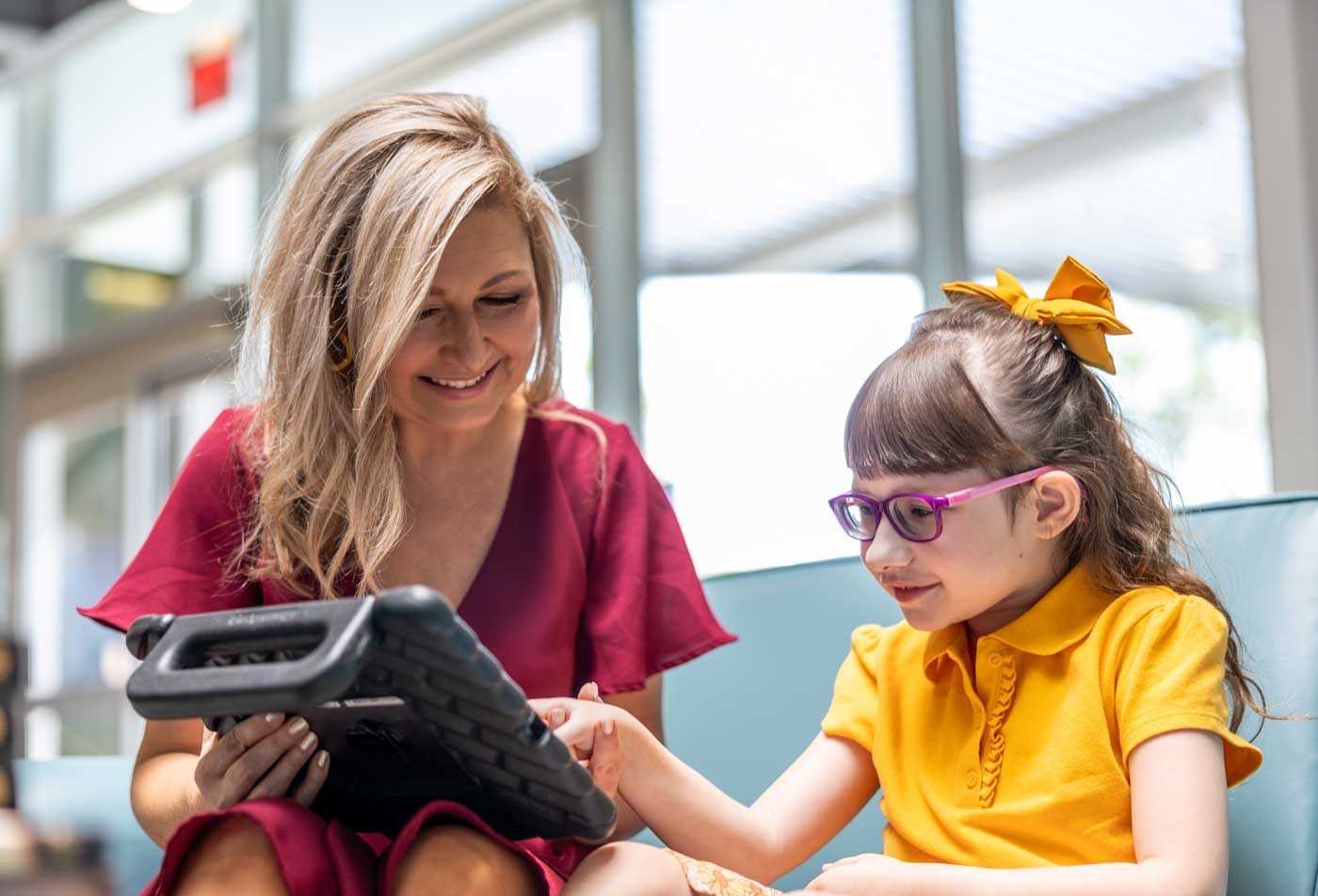 A teacher engages with a young girl with a communication tablet, demonstrating the skills learned in the certificate in Early Childhood Special Education