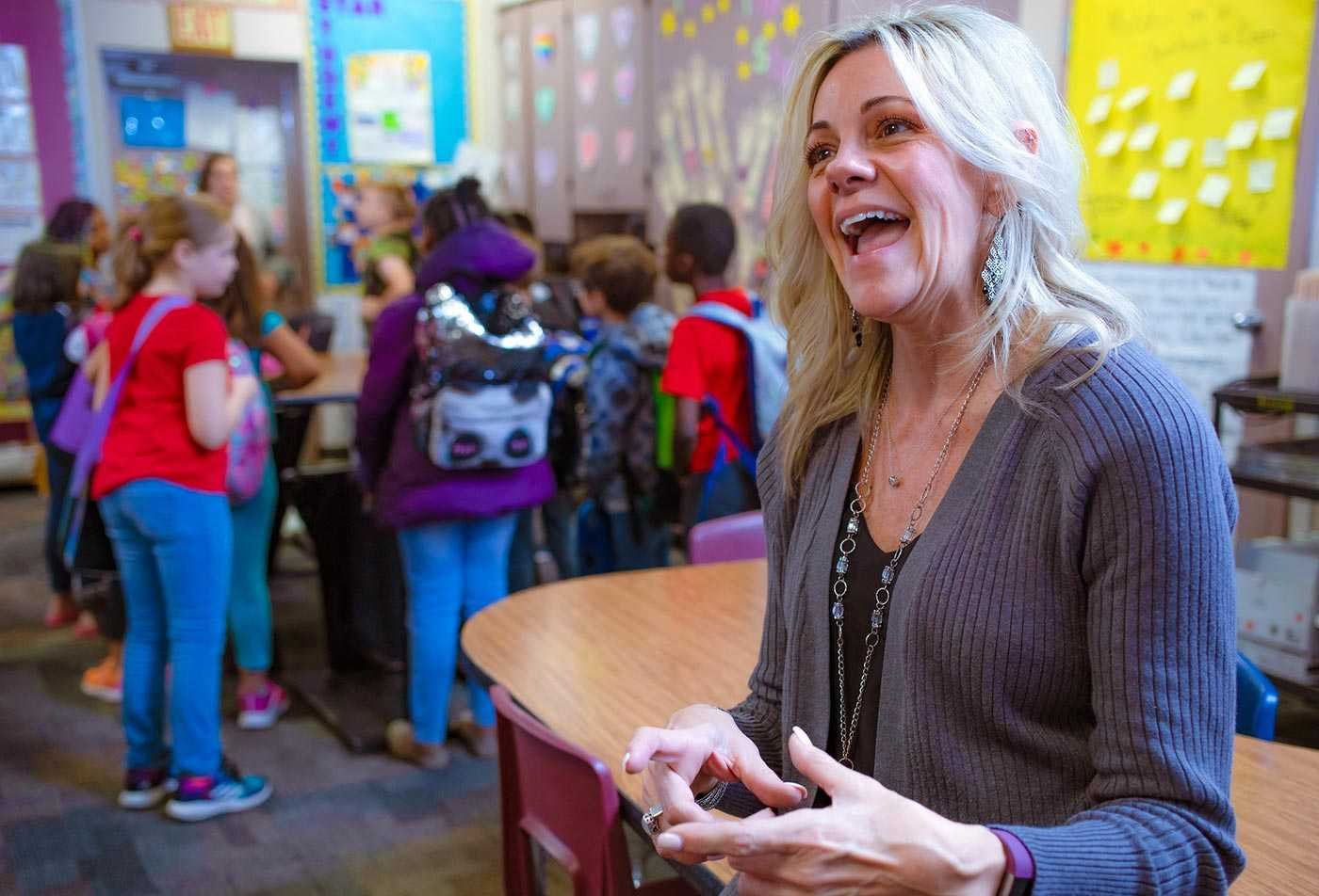A teacher enthusiastically presents in colorful classroom of children, demonstrating the expertise gained in the MEd in Elementary Education (Teacher Certification).