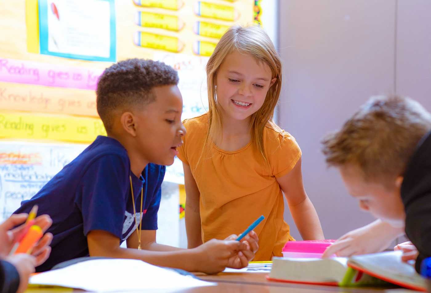 A group of children examine a book together, showcasing the field explored in the MED in Elementary Education.