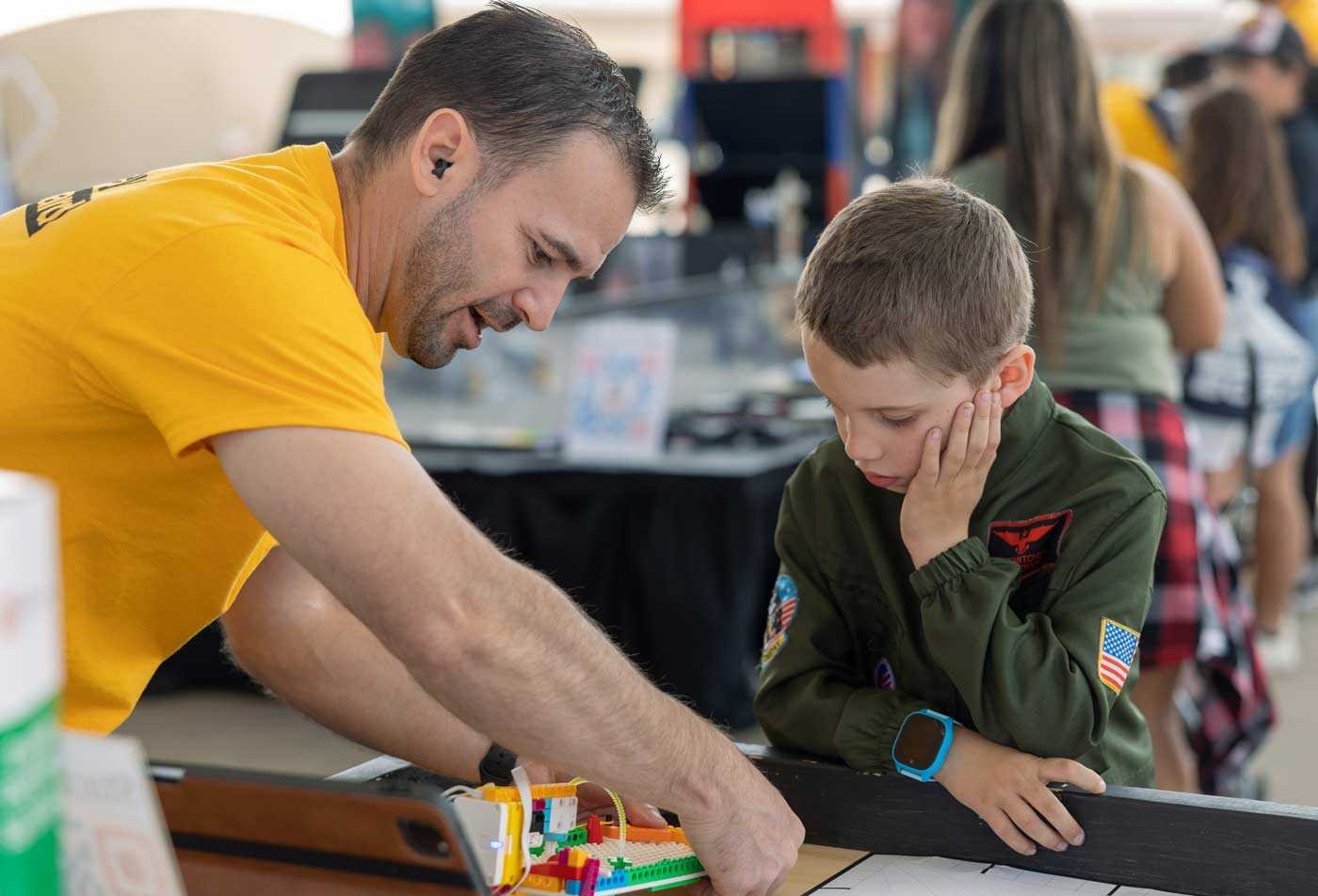 An instructor assists a young student with an engineering project, showcasing the expertise gained in the BAE in Educational Studies (Early Childhood Studies).