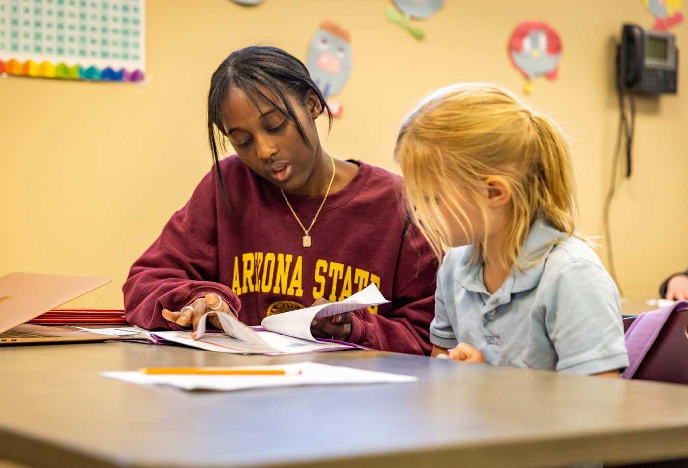 An ASU student helps a young child with an activity sheet in a classroom, practicing hands-on learning in the certificate in Bilingual Education and English as a Second Language.