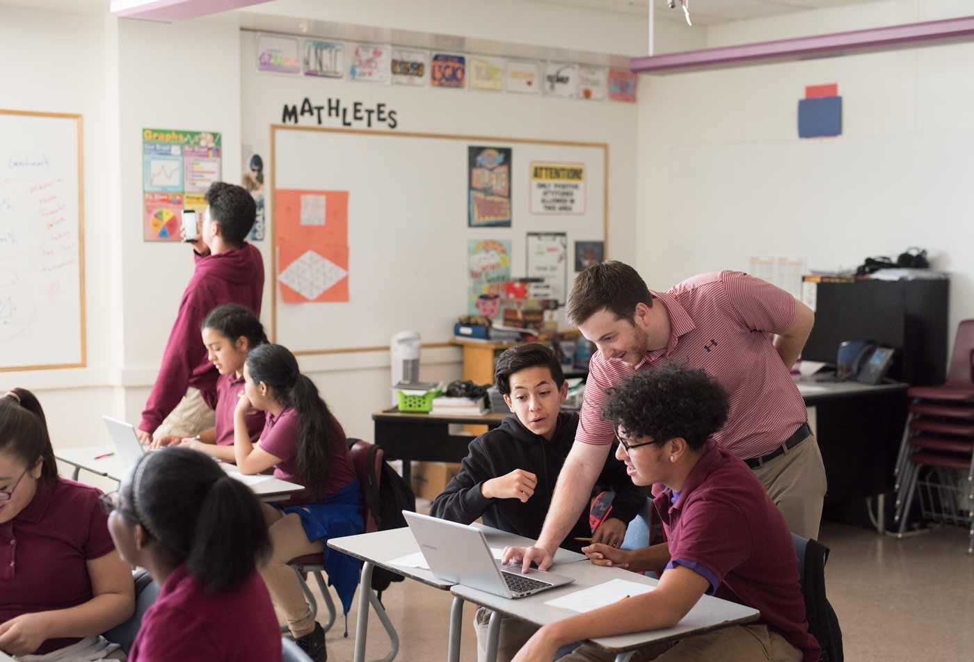 A teacher engages with students at their desk, demonstrating the skills learned in the BAE in Secondary Education (Mathematics).