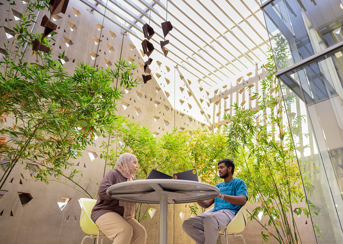 Two ASU students converse with their laptops in front of them in a shaded courtyard surrounded by greenery, exhibiting design-thinking in ASU's Public Health (Public Health Technology) master's degree program